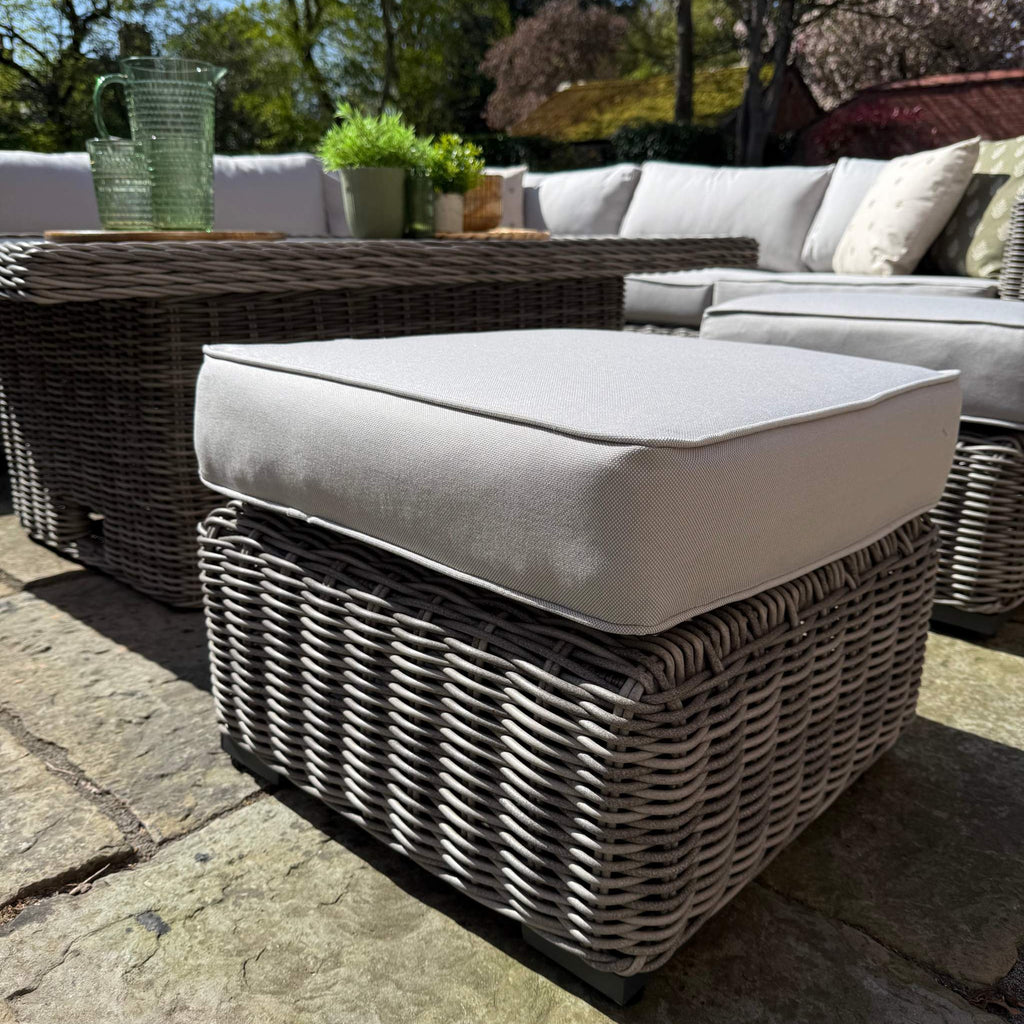 Outdoor patio furniture set with wicker chairs and ottoman on a stone patio.