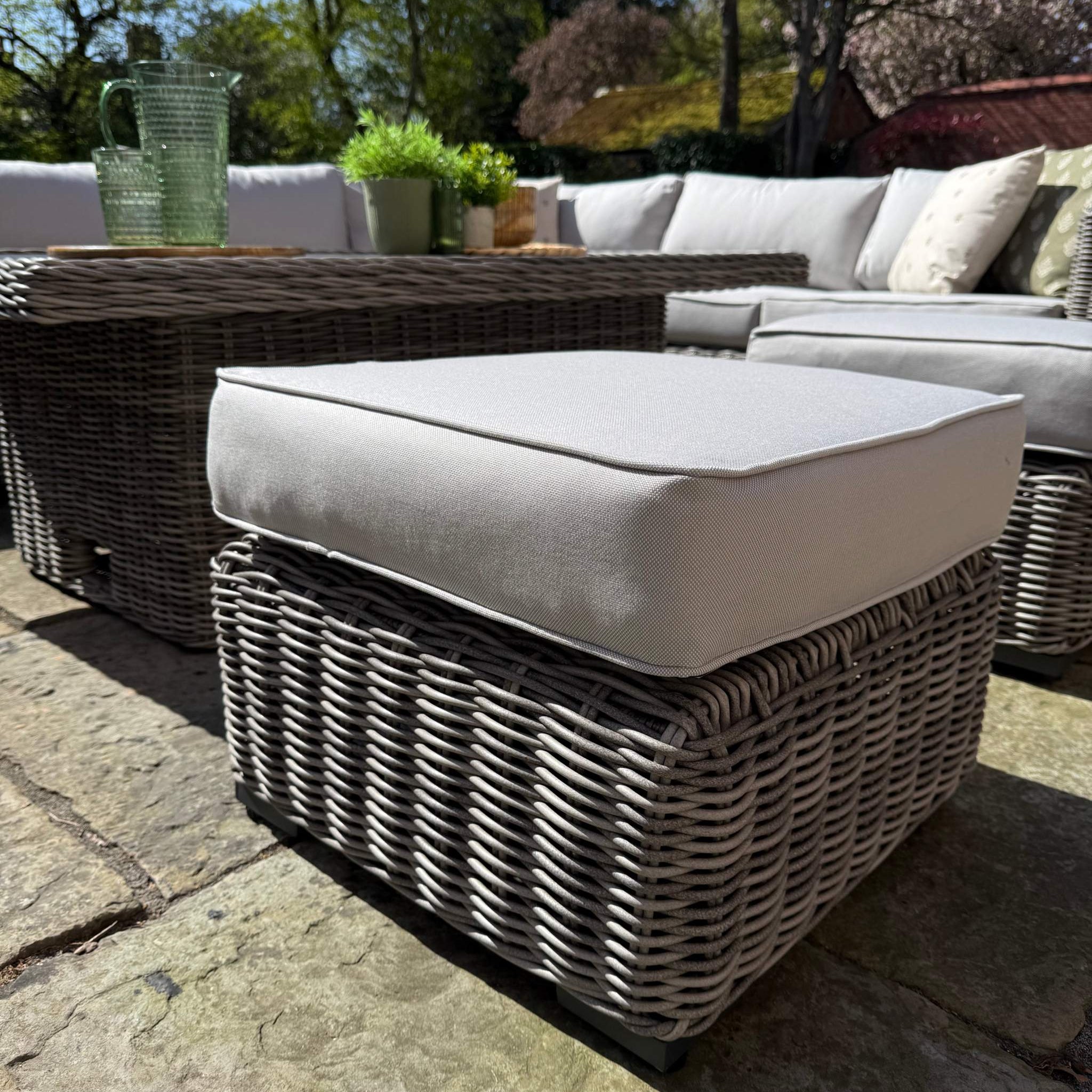 Outdoor patio furniture set with wicker chairs and ottoman on a stone patio.