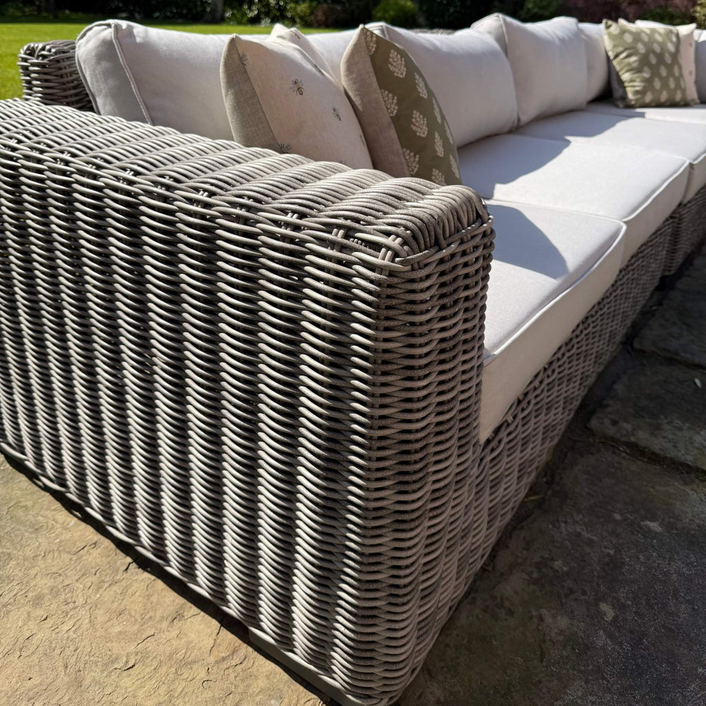 Outdoor wicker sofa with light grey cushions in a garden setting