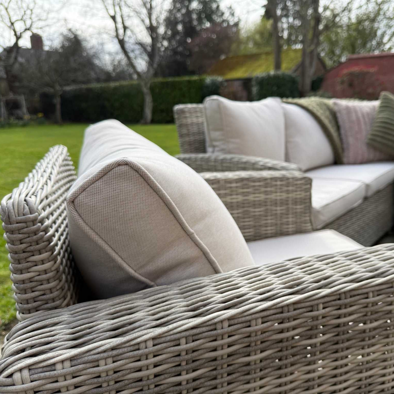Sienna Corner Rattan Garden Set with rising table, armchair, and footstools in natural rattan and neutral cushions outdoors