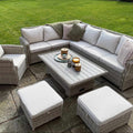 Sienna Corner Rattan Garden Set with rising table, armchair, and footstools in natural rattan and neutral cushions outdoors