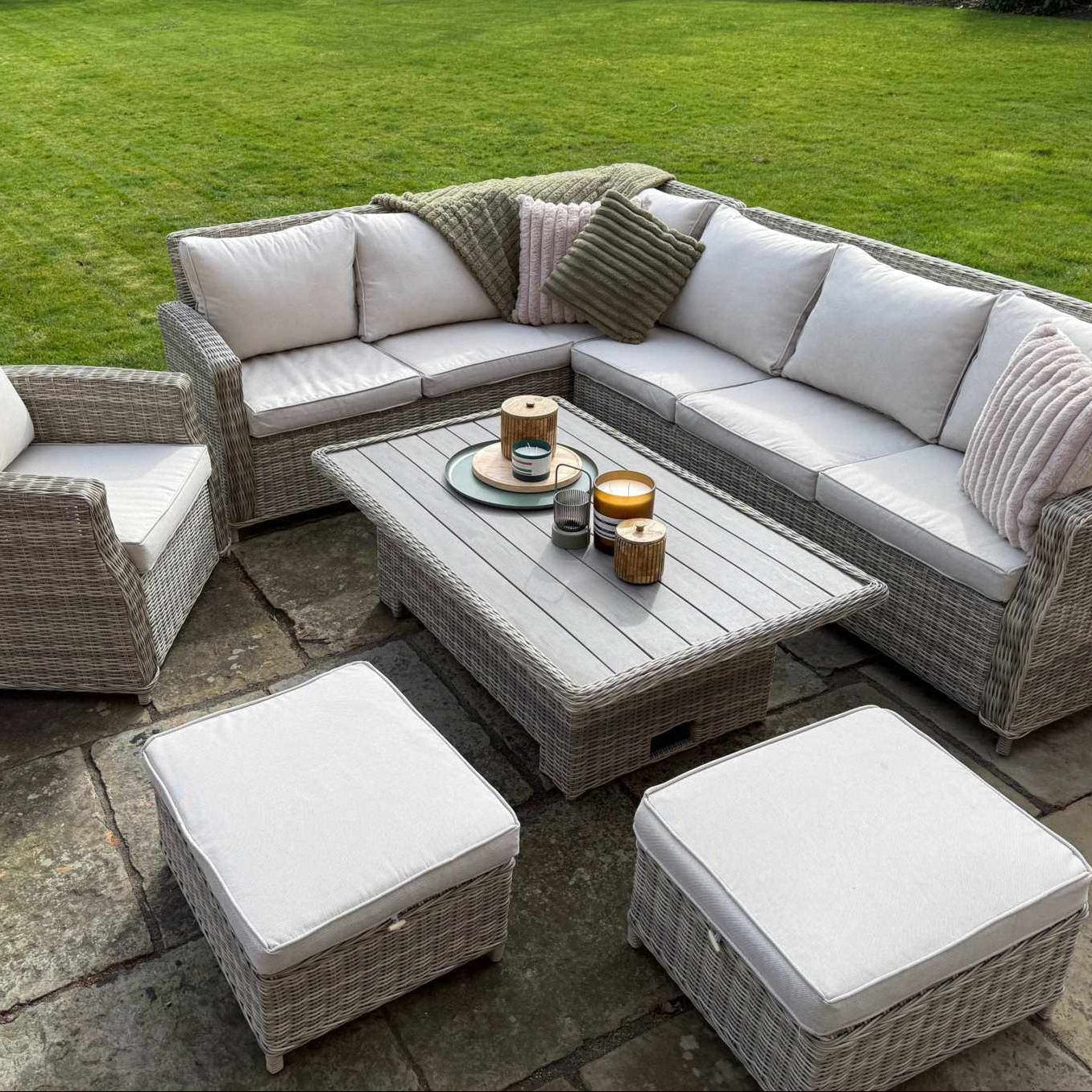 Sienna Corner Rattan Garden Set with rising table, armchair, and footstools in natural rattan and neutral cushions outdoors