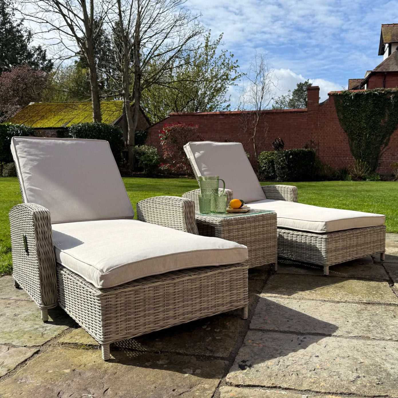Sienna Twin Sun Lounger Set with cream cushions and glass top table in natural rattan weave outdoors